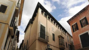 Façade en angle d’un immeuble ancien dans une ruelle, architecture méditerranéenne et volets verts sous un ciel partiellement nuageux