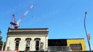 Façade ancienne surmontée d’une grue rouge et blanche sous un ciel bleu, photographie d’architecture urbaine.