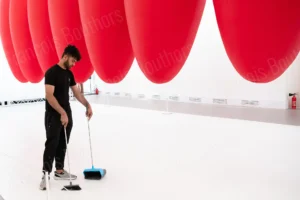 Photographie de rue d’un homme balayant le sol sous une installation rouge monumentale – François Bouthors