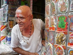 Photographie de portrait d’un homme âgé dans une boutique en Inde entouré d’images religieuses, par François Bouthors.
