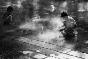 Street photo en noir et blanc de deux enfants jouant dans la vapeur sur une place urbaine, instant spontané capturé par François Bouthors.